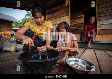 Myanmar, Asia, madre e figlia la cottura di alimenti di mare e la nonna è li guarda. Foto Stock