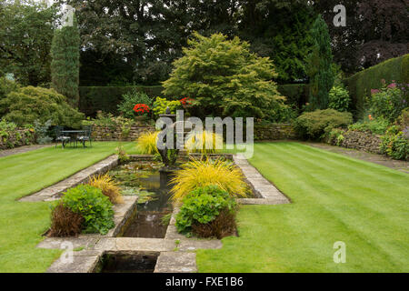 Una bella, privato tradizionale, paesaggistico, country Garden, West Yorkshire, Inghilterra - laghetto ornamentale, fontana, area con posti a sedere e prato a strisce. Foto Stock