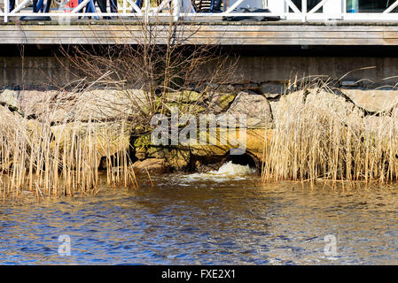 Tempesta di uscita di scarico in un fiume con nei dintorni di blocchi di pietra e parte di un molo o ponte al di sopra. Foto Stock