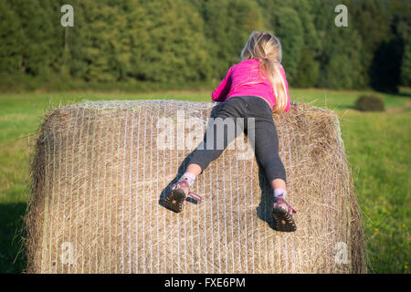 Bambino ragazza bionda da paglia balla di fieno in campo, prato, giocare i bambini attività estive Foto Stock