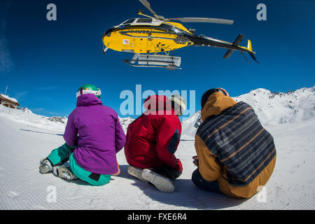 Un gruppo di sciatori e snowboarder sono riaccompagnati in elicottero in cima a una montagna nelle Alpi francesi. Foto Stock