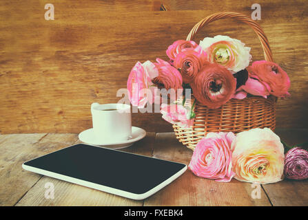 Tazza di caffè accanto al tablet e fiori su un tavolo di legno. vintage filtrato e tonica Foto Stock