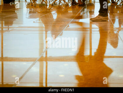 Riflessioni di sagome delle gambe, piedi e la parte inferiore del corpo parti di viaggiatori occupato in un aeroporto /atrio della stazione. Colori caldi. Foto Stock