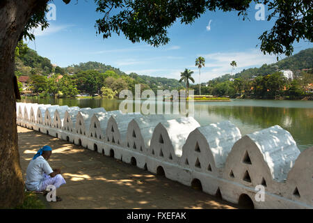 Sri Lanka, Kandy, Dalada Vidiya, uomo seduto in ombra accanto a Kiri Muhuda Lago Foto Stock