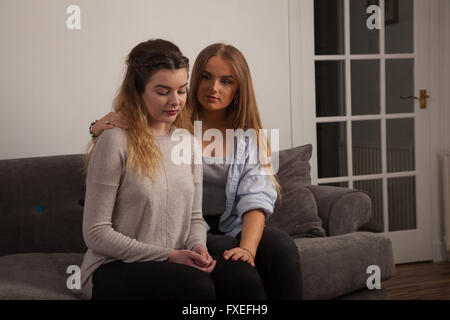Due giovani donne confortarci vicendevolmente a casa su un divano. Foto Stock
