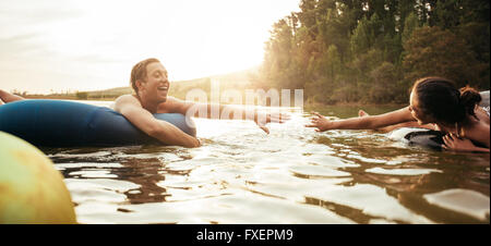 Amorevole coppia giovane circa per tenere le mani mentre galleggiante su tubi interni nel lago. Giovane uomo e donna su un tubo gonfiabile in wate Foto Stock