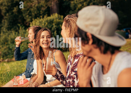 Ritratto di felice giovani seduta da un lago con birre. Gruppo di amici appendere fuori a lago. Foto Stock