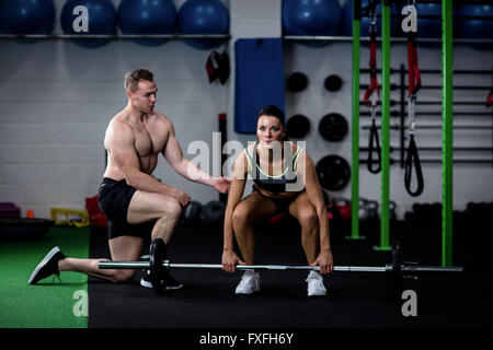 Il trainer di istruire una donna durante il sollevamento barbell Foto Stock