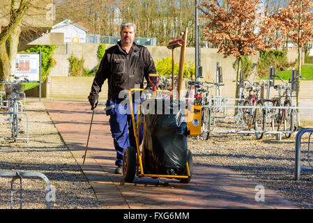 Lund, Svezia - 11 Aprile 2016: il lavoro uomo a camminare verso di voi con la garbage carrello e strumento per prelevare i rifiuti dalla strada. Un Foto Stock