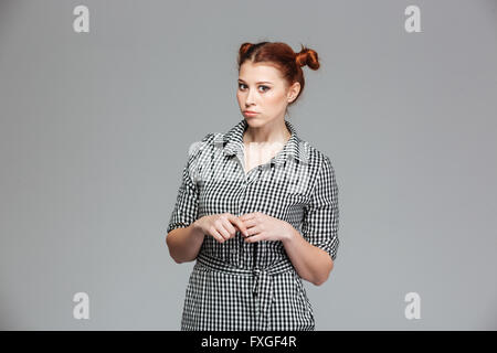 Grave funny giovane donna in maglia a scacchi in piedi su sfondo grigio Foto Stock