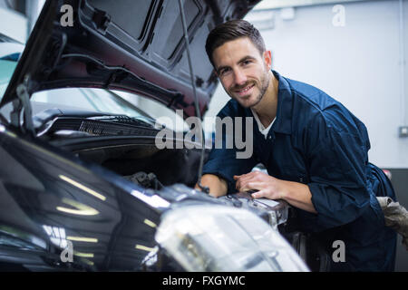 Mechanic sorridente alla telecamera mentre esaminando auto motore Foto Stock