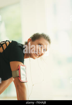 Donna sorridente con cuffie e lettore mp3 armband in palestra Foto Stock