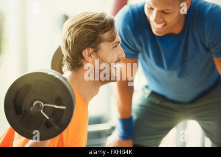 Personal trainer incoraggiando l'uomo facendo barbell squat in palestra Foto Stock
