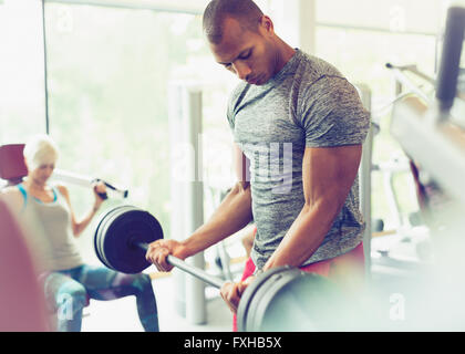 Focalizzato l'uomo facendo barbell bicipite riccioli in palestra Foto Stock