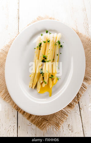 Cucinati freschi Asparagi bianchi con il burro fuso e il prezzemolo tritato su una piastra Foto Stock