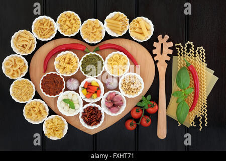 La pasta italiana e mediterranea ingredienti alimentari su un cuore tavola sagomata in porcellana bocce su legno scuro dello sfondo. Foto Stock