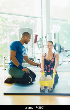 Personal trainer donna guida allungamento gambe con banda di resistenza in palestra Foto Stock