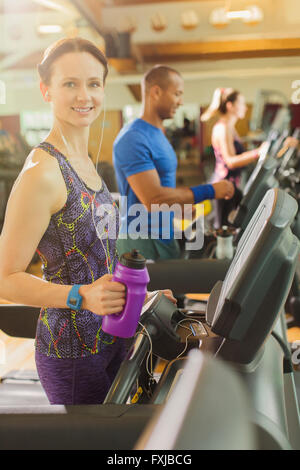 Ritratto di donna sorridente con bottiglia di acqua sul tapis roulant in palestra Foto Stock