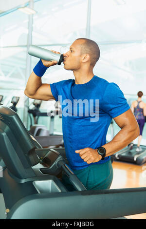 Uomo di bere acqua sul tapis roulant in palestra Foto Stock