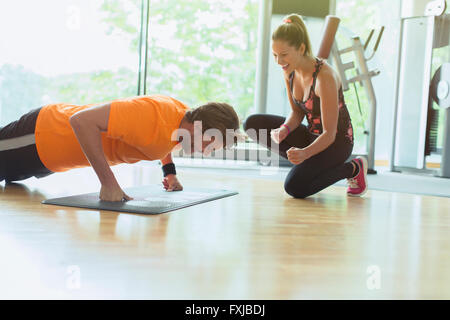 Personal trainer a fare il tifo per l'uomo fare push-up in palestra Foto Stock