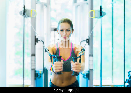 Donna focalizzata tramite il cavo attrezzature per esercizi in palestra Foto Stock