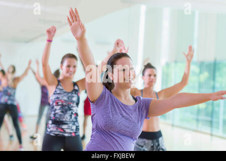 Donna sorridente con le braccia sollevate nella classe di esercizio Foto Stock