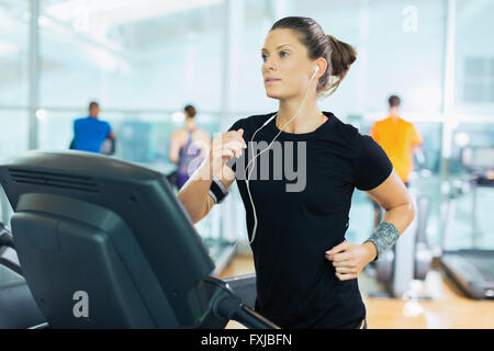 Donna focalizzato in esecuzione sul tapis roulant con cuffie in palestra Foto Stock