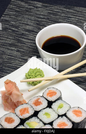 Rotoli maki sushi e zenzero con wasabi su una piastra. In fondo è una ciotola con la salsa di soia e bastoncini. Verticalmente. Foto Stock