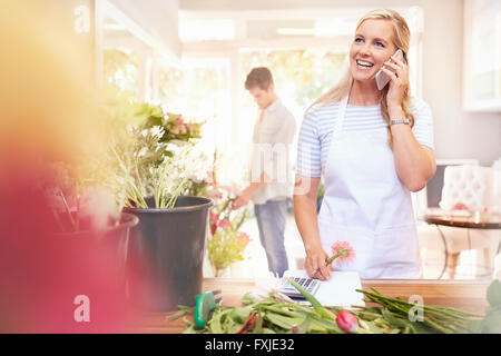 Fiorista sorridente parlando al cellulare nel negozio di fiori Foto Stock