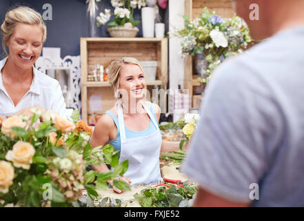 Fioristi disponendo bouquet e parlare con il cliente in negozio di fiori Foto Stock