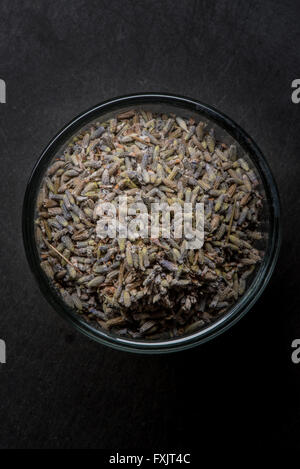 Lavanda essiccata in recipiente di vetro sul nero ardesia Tagliere sfondo Foto Stock