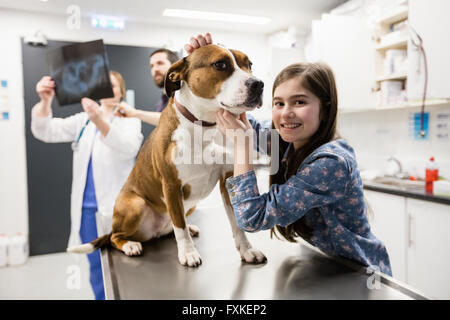 Ragazza che gioca con il suo cane mentre vet discutendo x-ray in background Foto Stock