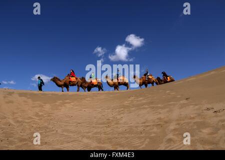 Jiuquan, la Cina della provincia di Gansu. Xvi Apr, 2016. Persone corsa cammelli al Crescent Lake scenario spot in montagna Mingsha di Dunhuang City, a nord-ovest della Cina di Provincia di Gansu, Aprile 16, 2016. Dunhuang City ha dimostrato la sua naturale bellezza dopo una pioggia di Sabato. Credito: Zhang Xiaoliang/Xinhua/Alamy Live News Foto Stock