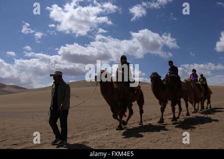 Jiuquan, la Cina della provincia di Gansu. Xvi Apr, 2016. Persone corsa cammelli al Crescent Lake scenario spot in montagna Mingsha di Dunhuang City, a nord-ovest della Cina di Provincia di Gansu, Aprile 16, 2016. Dunhuang City ha dimostrato la sua naturale bellezza dopo una pioggia di Sabato. Credito: Zhang Xiaoliang/Xinhua/Alamy Live News Foto Stock