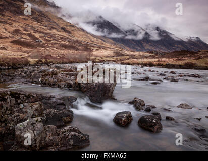 La Aonach Eagach ridge covava con bassa giacente cloud come il fiume Coe cascades sopra le cascate che corre al di sotto di esso. Foto Stock