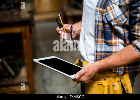 Carpenter utilizzando digitale compressa in officina Foto Stock