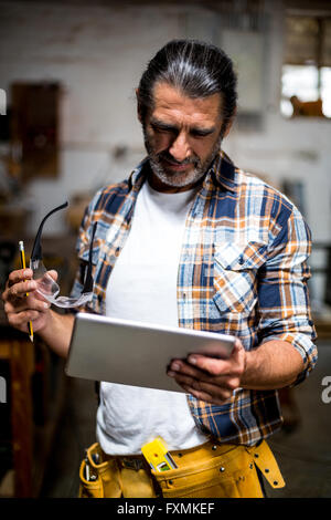 Carpenter utilizzando digitale compressa in officina Foto Stock