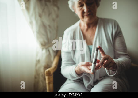 Senior donna che mantiene un livello di glucosio nel sangue monitor Foto Stock