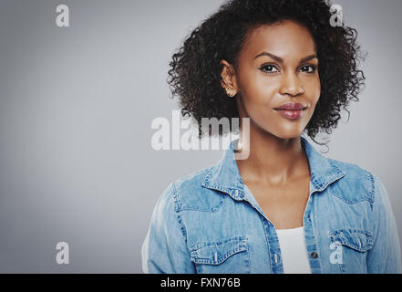 Fiducioso bella donna nera con blu jean shirt su sfondo grigio Foto Stock