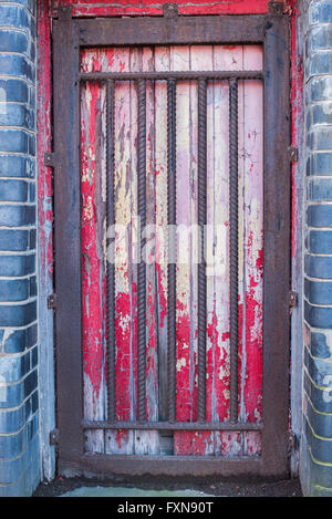 Di ferro arrugginito griglia sopra porta rossa con peeling paint Foto Stock