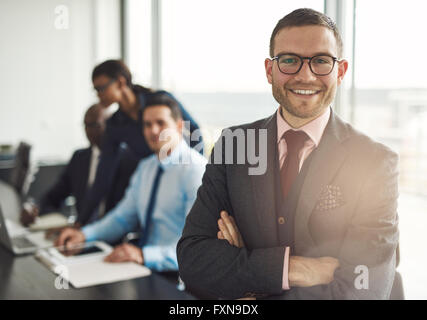Fiducioso sorridente business executive con bracci ripiegati vicino al tavolo da conferenza con tre colleghi parlare di qualcosa in grande Foto Stock