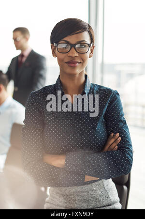 Sorridente business woman executive con fiduciosa espressione e bracci ripiegati vicino al tavolo da conferenza con i colleghi in un grande e luminoso Foto Stock