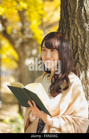 Giovane donna giapponese con libro in un parco della città Foto Stock