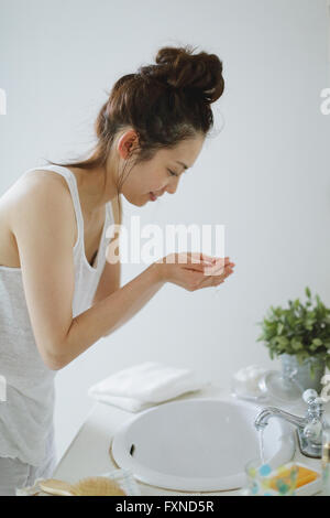 Attraente giovane donna giapponese faccia il lavaggio in bagno Foto Stock