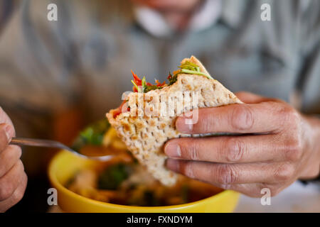 Mano d'uomo in possesso di un mezzo mangiato flatbread panino su una ciotola di zuppa Foto Stock