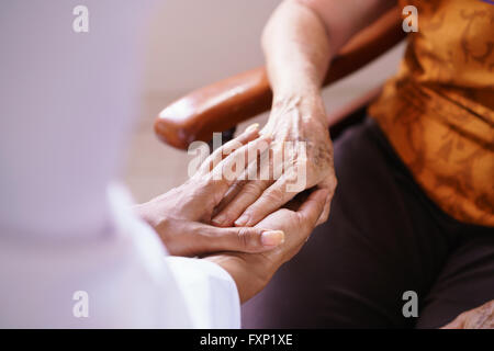 Anziani in ospizio geriatrico: Nero medico visita un paziente invecchiato, tenendo le mani di una donna senior. Concetto di comfort e Foto Stock