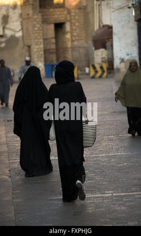 La donna vestita di nero tradizionale abaya passeggiando attraverso AlBalad, la vecchia città di Jeddah, Arabia Saudita Foto Stock