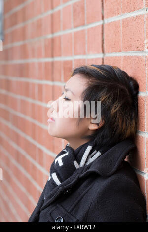 Asian donna americana appoggiata contro un muro di mattoni Foto Stock