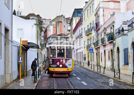 Famoso tram linea 28 fermandosi in una stradina nel quartiere di Alfama a Lisbona, in Portogallo la mattina presto con le persone Foto Stock