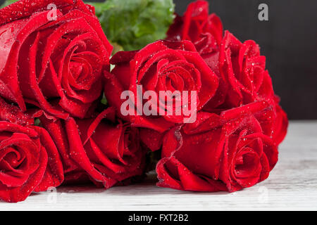 Bouquet di rose rosse con acqua gocce di rugiada sul bianco rustico in legno tavolo. Profondità di campo. Foto Stock